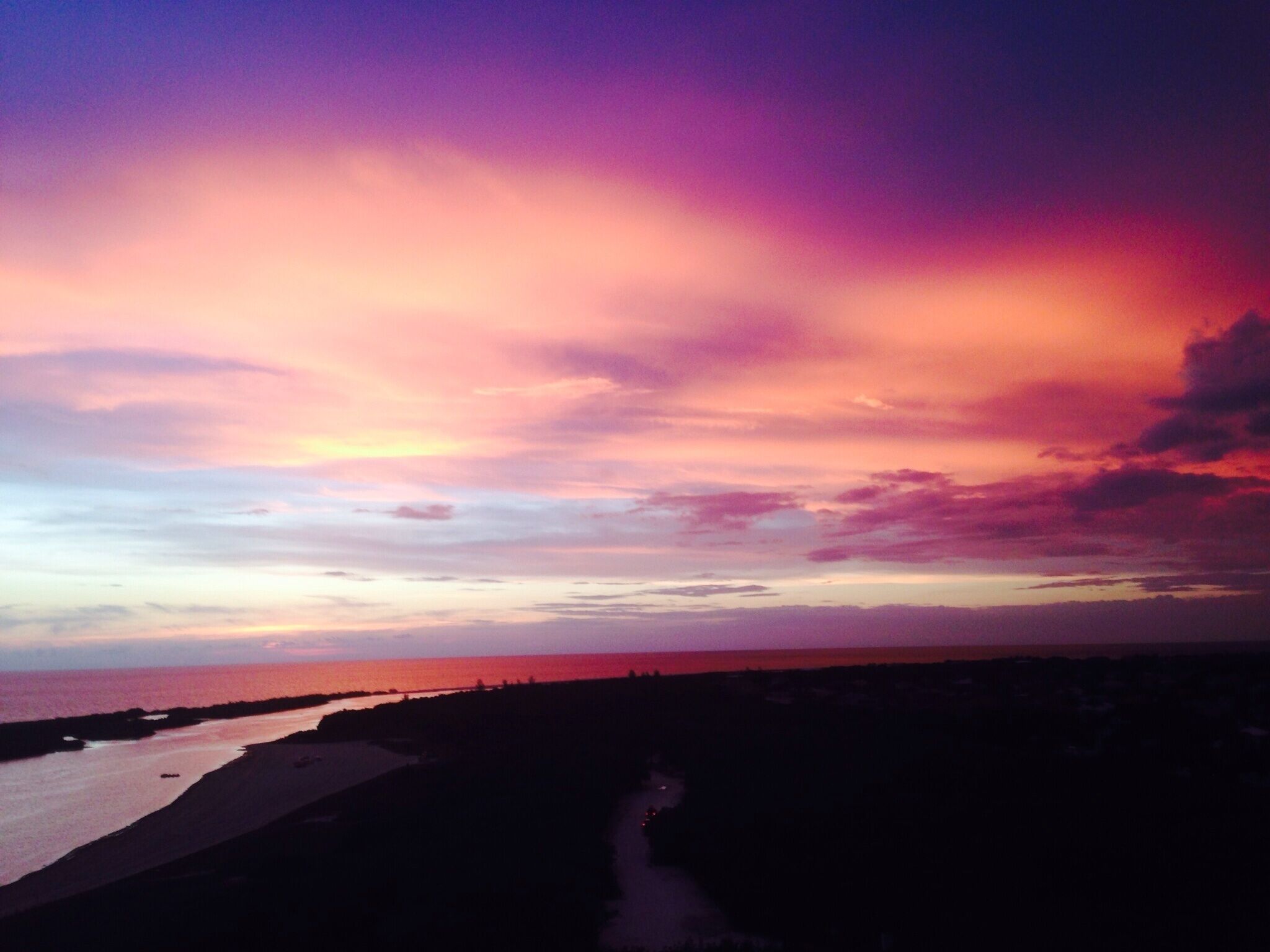 Un coucher de soleil sur la côte, avec une plage et une route menant à la mer.