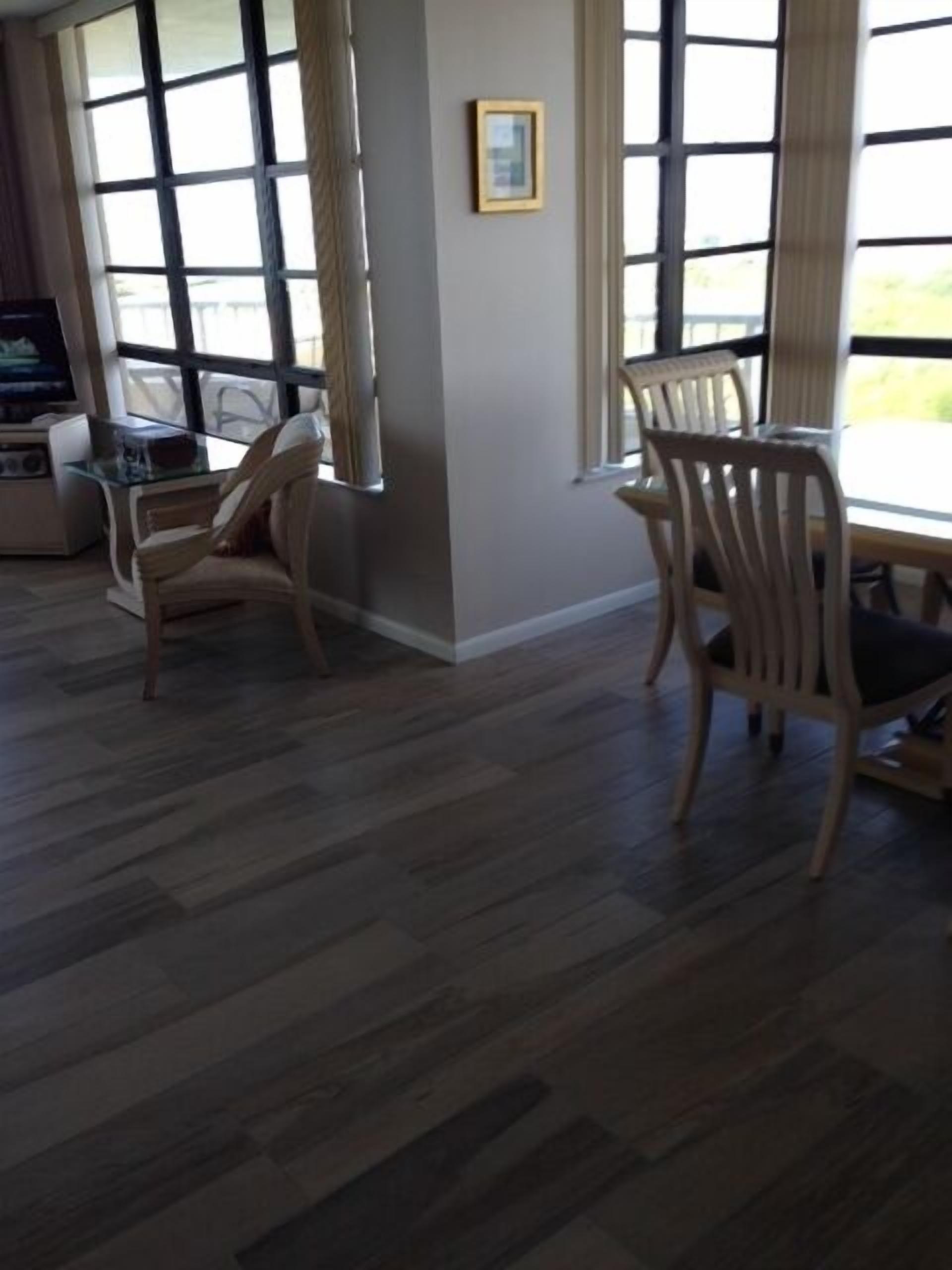 A room with a large window, a wooden floor, and a dining area with chairs.