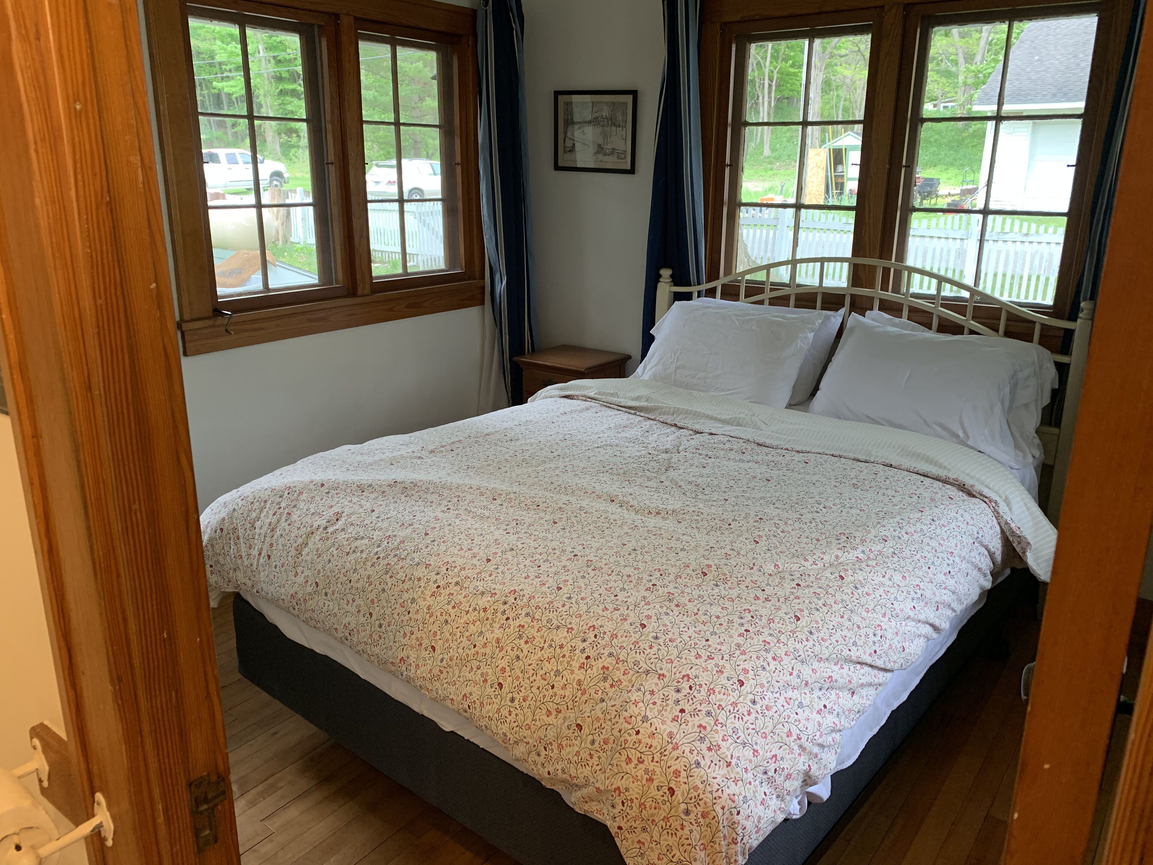 Camera da letto con un letto, una testiera in legno e una finestra che si affaccia su un recinto bianco a maglie e vegetazione.
