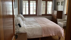 A bedroom with a bed, dresser, and two windows with curtains. - Sandy Beach Cottage on Torch Lake, in Alden (Alden)