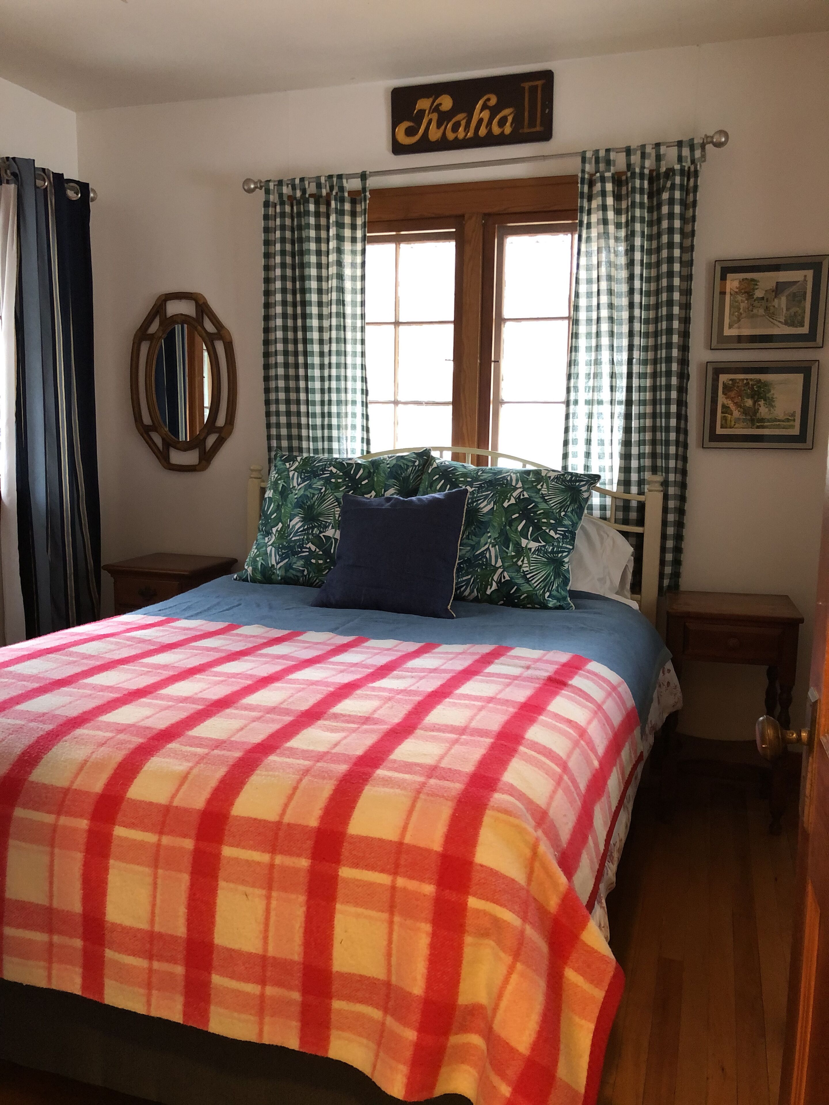 Un dormitorio con cama, ventana con cortinas, un letrero en la pared, un espejo y dos cuadros enmarcados.