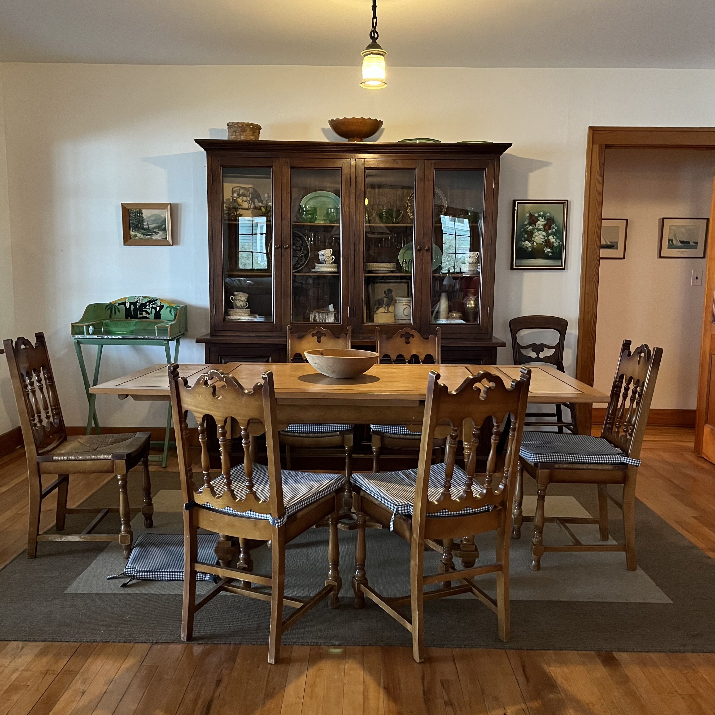 A dining room with a wooden table, six chairs, a cabinet with glass doors, and a hanging light fixture.