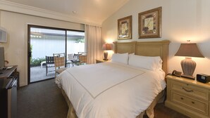 A hotel room with a large bed, two bedside lamps, a desk with a telephone, and a view of an outdoor patio with a chair and table. - Getaway Suite at Silverado in Napa (Napa)