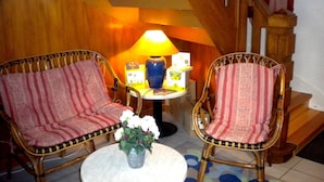 Une pièce avec deux fauteuils en osier, une petite table sur laquelle se trouve un vase de fleurs, une lampe et une boîte.