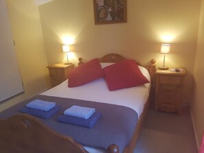 A neatly made bed with red and blue pillows, two bedside tables with lamps, and a wooden headboard.