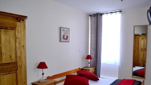 Une chambre à coucher avec un lit en bois, deux tables de chevet avec des lampes, une armoire, une fenêtre avec des rideaux et un tableau encadré accroché au mur.