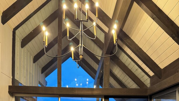 Un espace repas comprenant une table et des chaises en bois, un lustre et de grandes fenêtres donnant sur l’extérieur.