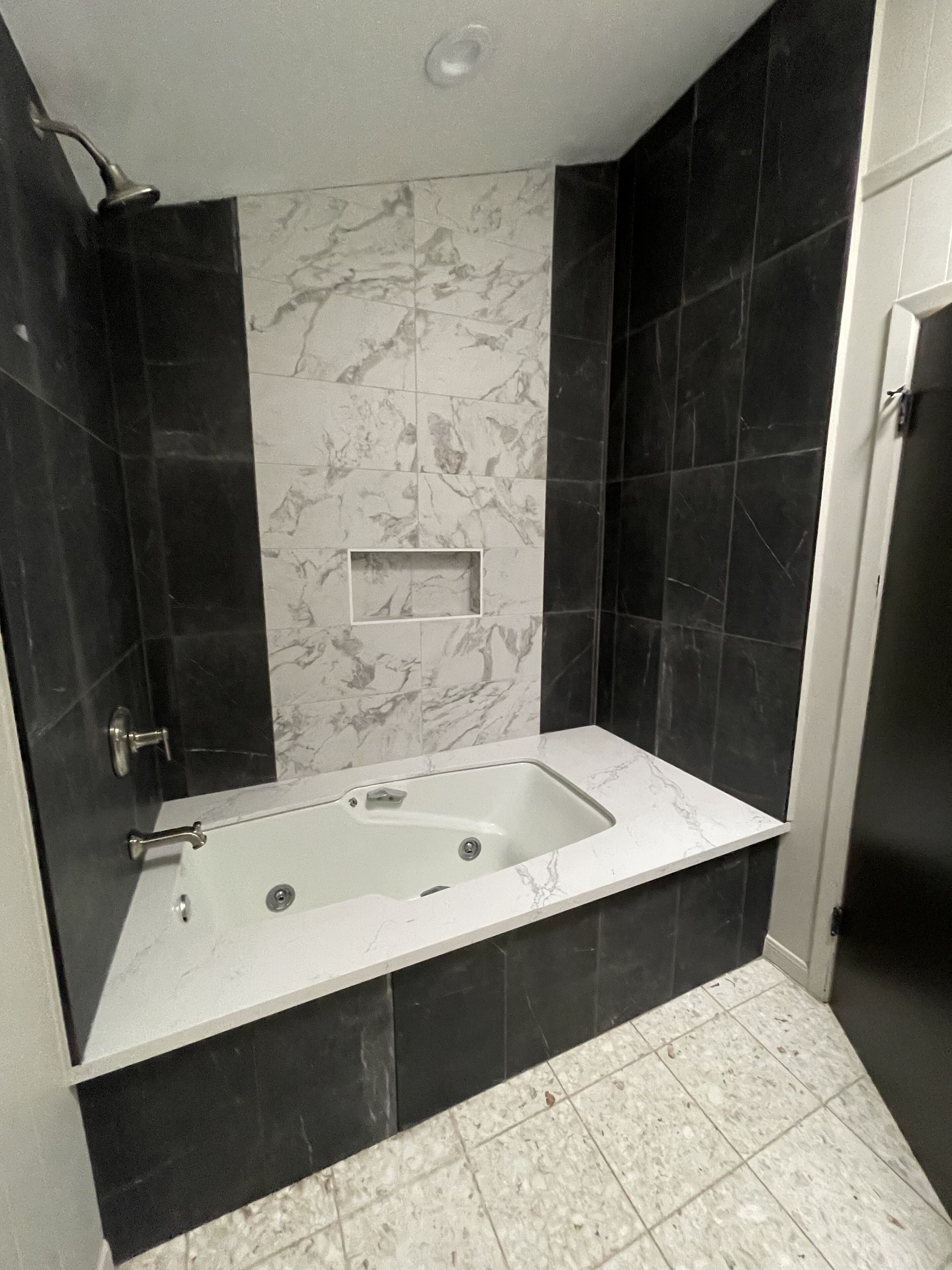 A bathroom with a freestanding bathtub, black and white marble tiles, and a small shelf above the tub.