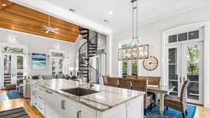 A spacious kitchen with a large island, a wooden ceiling, and a dining area with wicker furniture. - Sandy Souls Cottage & CH - NEWLY RENOVATED! GULF VIEWS! ACCESS TO FITNESS/TENNIS (Rosemary Beach)