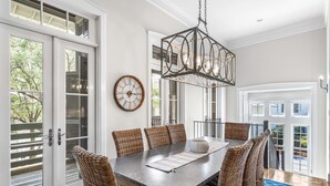 A dining area with a large table, wicker chairs, a hanging light fixture, and a clock on the wall. - Sandy Souls Cottage & CH - NEWLY RENOVATED! GULF VIEWS! ACCESS TO FITNESS/TENNIS (Rosemary Beach)