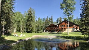 Uma cabana com um lago, rodeada por árvores, e um alpendre com cadeiras.