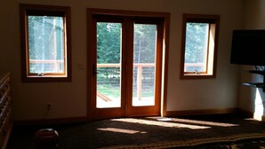 Um quarto com três janelas, uma porta de madeira, um tapete e uma televisão sobre um suporte.
