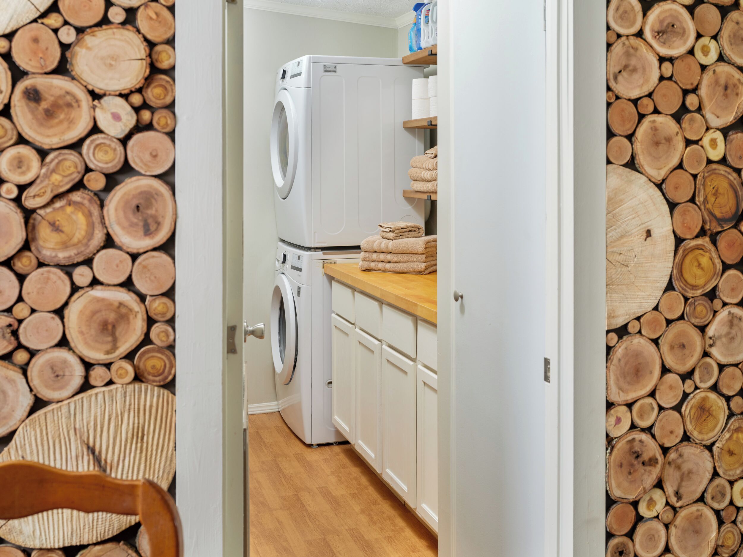 Een wasserij met een wasmachine en droger, houten balken aan de wanden en een houten aanrechtblad met handdoeken.