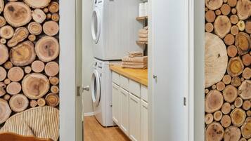 Een wasserij met een wasmachine en droger, houten balken aan de wanden en een houten aanrechtblad met handdoeken.