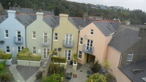 A row of terraced houses with balconies, a small garden area, and a hilly background.