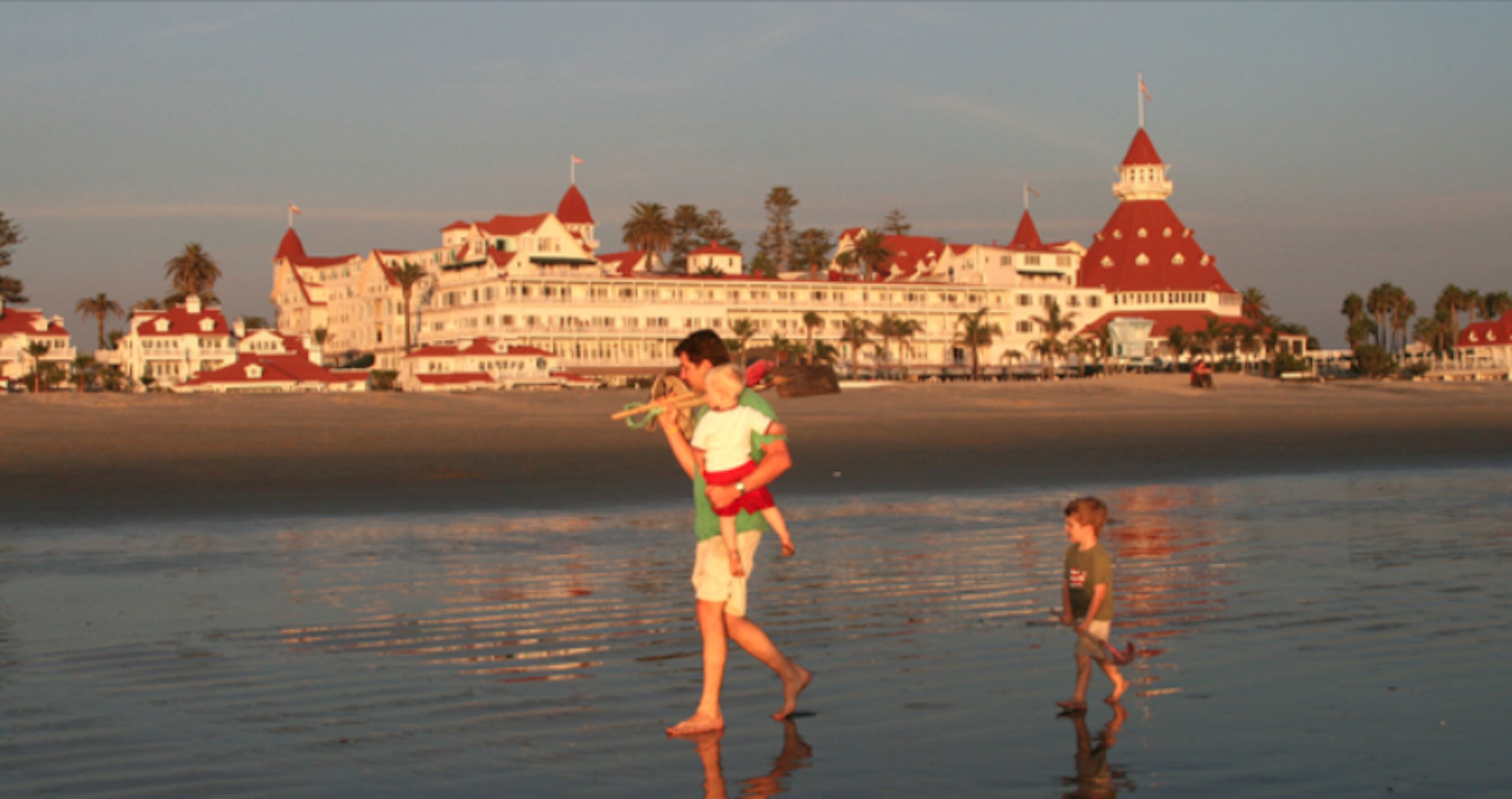 A beachfront hotel with multiple red-roofed buildings, palm trees, and a sandy beach.