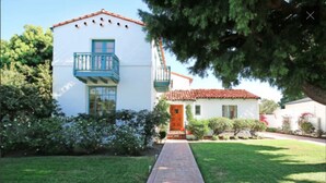 A two-story house with a red-tiled roof, a front porch, and a pathway leading to the entrance. - Elegant Garden Apartment (Coronado)