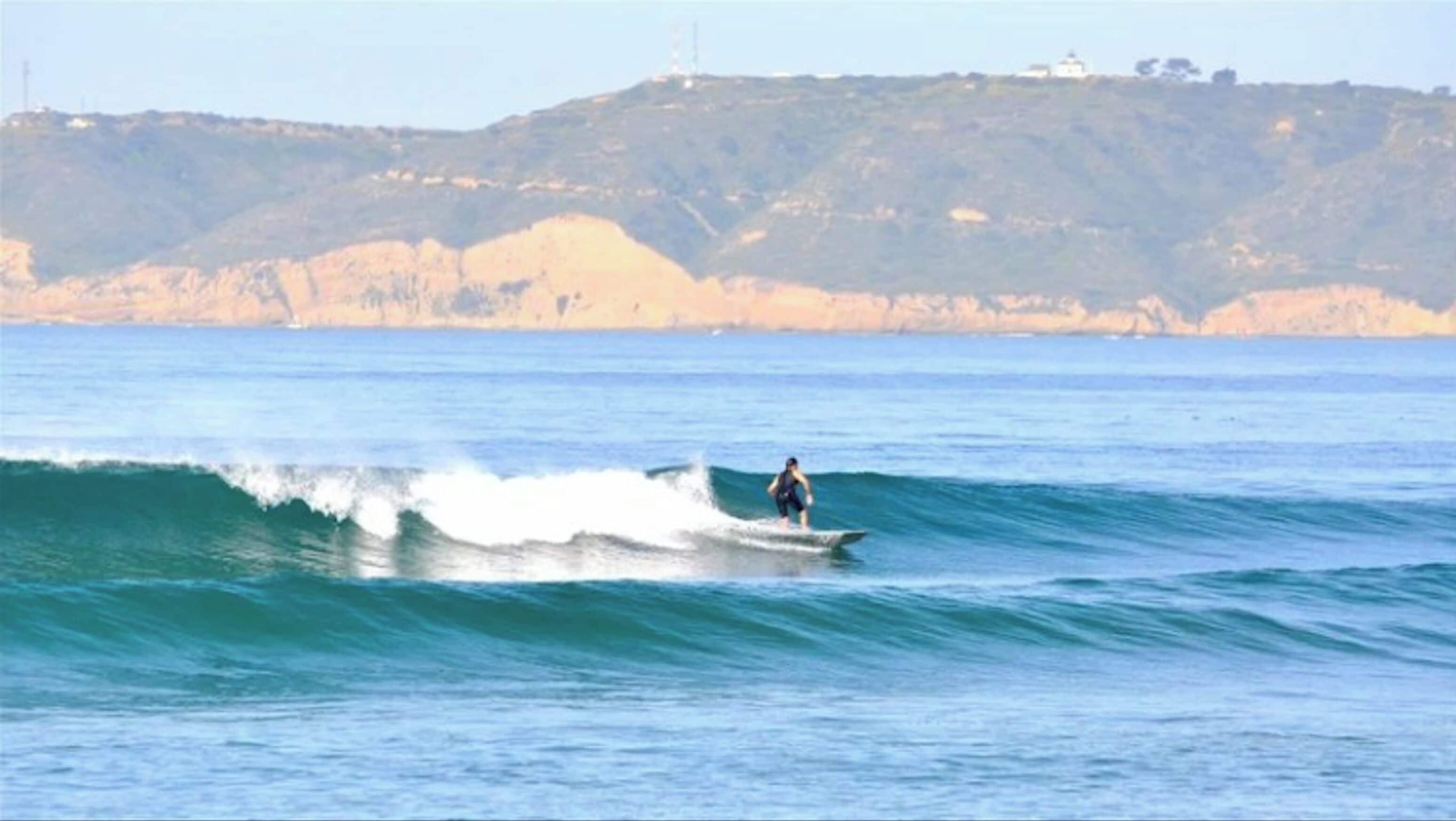 A person surfing on a wave with a coastal landscape in the background.
