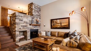 A living room with a stone fireplace, a leather sofa, a wooden coffee table, and a painting on the wall. - Spacious Mountain Townhouse. Great Location! (Breckenridge)