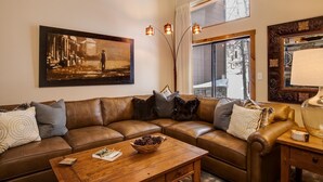 A living room with a brown leather sofa, a wooden coffee table, and a painting on the wall. - Spacious Mountain Townhouse. Great Location! (Breckenridge)