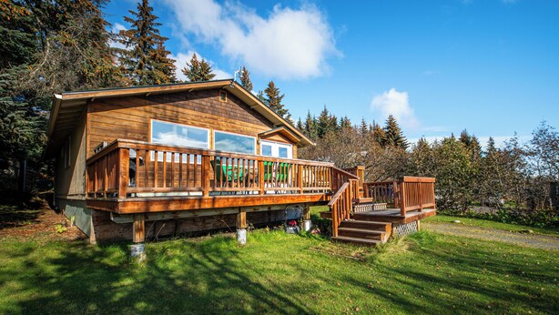 Een houten chalet met een terras, grote ramen en een trap naar een veranda.