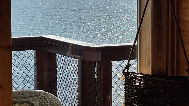 Un balcón de madera con vista a un lago tranquilo y montañas nevadas.