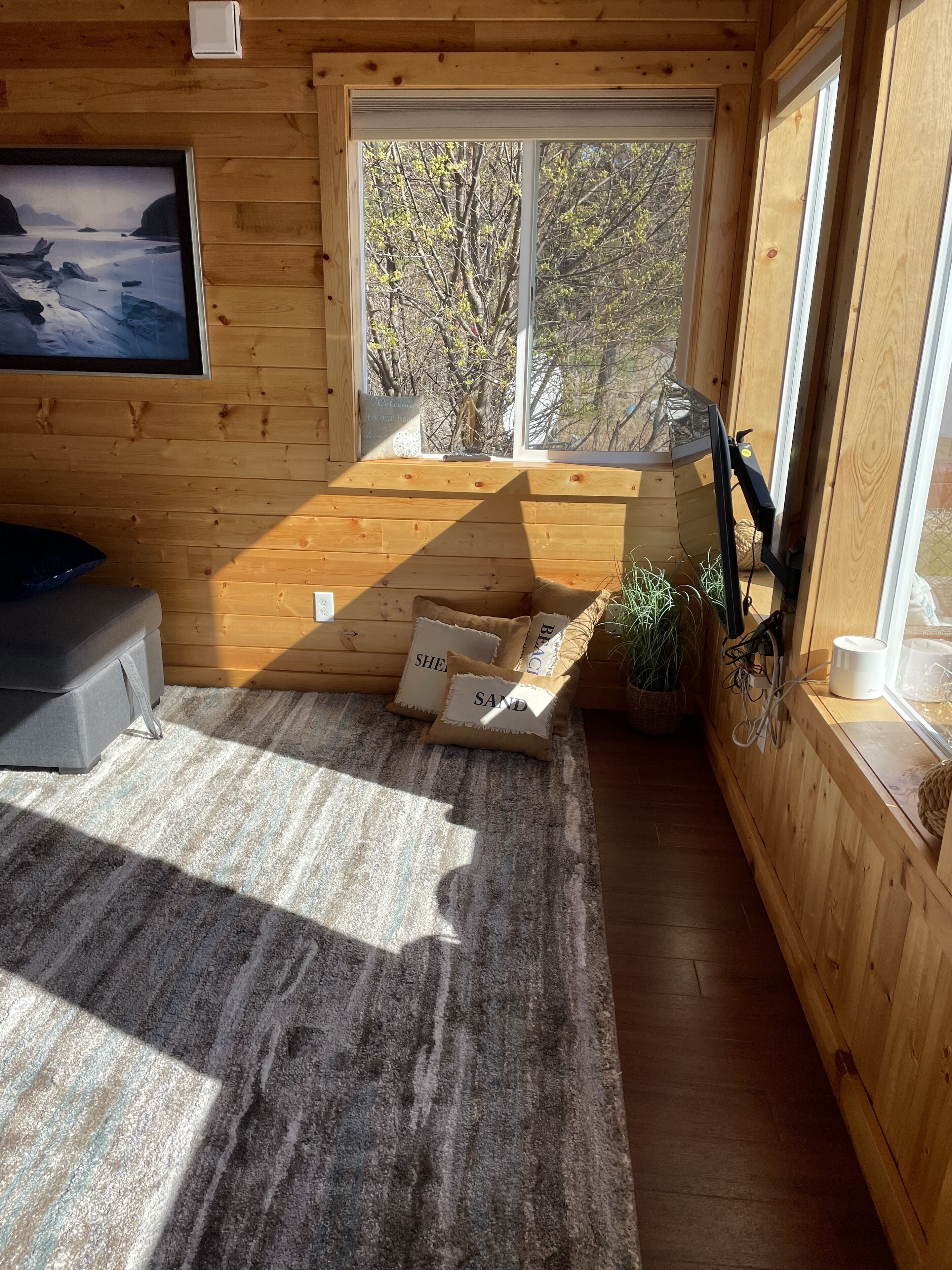 Ein gemütliches Blockhäuschen-Zimmer mit großem Fenster, einem Bett, einem Fernseher und einem kleinen Tisch mit einer Pflanze.