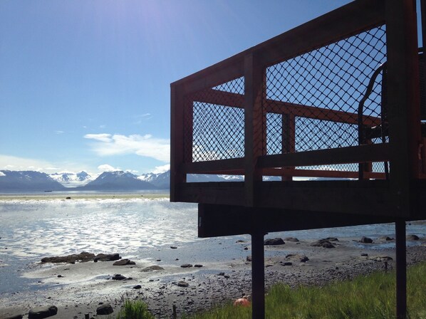 A view of a lake with mountains in the background, a wooden structure with a mesh roof, and a rocky shoreline. - Homer Beachside cabins (Homer)