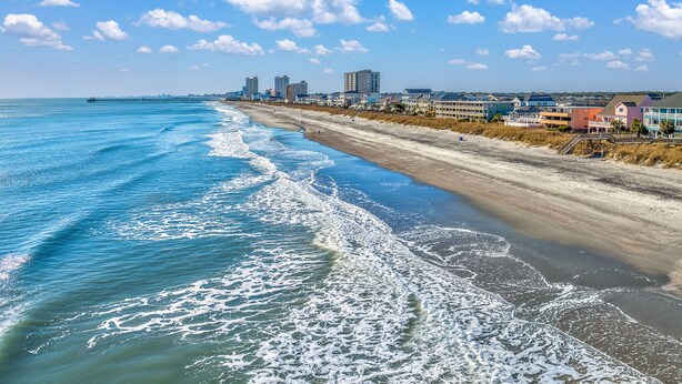 A beach with a pier extending into the ocean, buildings along the shore, and a clear sky. - Affordable cozy 2 bedroom condo 1st floor screened in patio in gated community. (North Myrtle Beach)