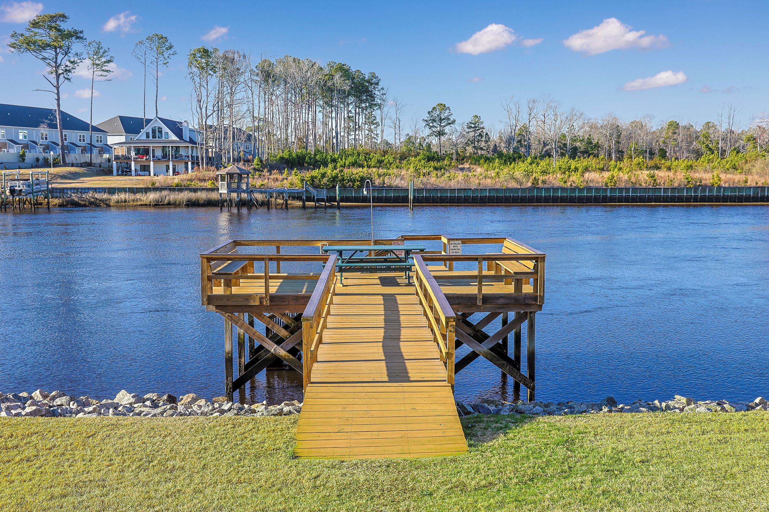 A wooden dock leading to a small wooden structure by a calm lake, surrounded by houses and trees.