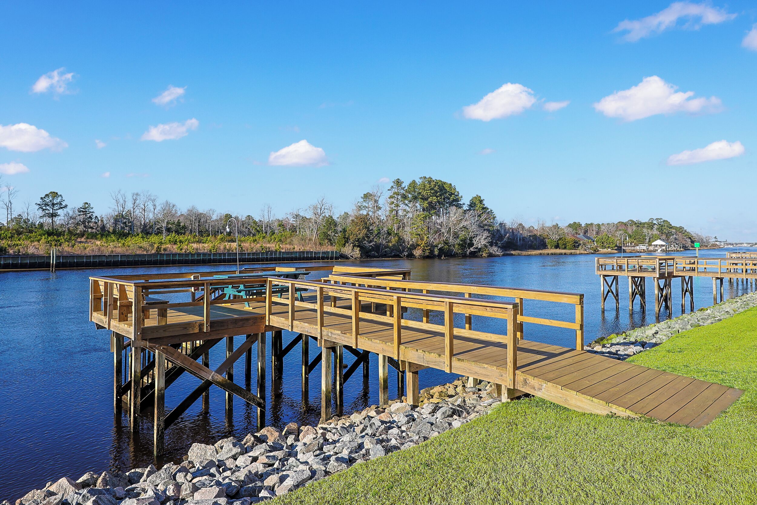 A wooden dock extending into a calm body of water, with a grassy area and rocky shoreline in the foreground.