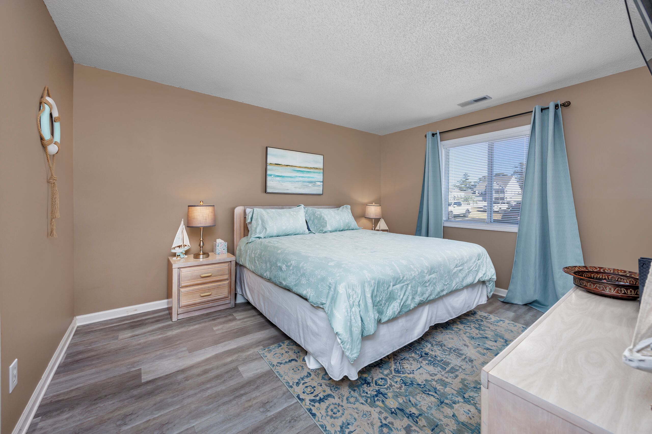 A bedroom with a bed, bedside tables, a lamp, a window with curtains, and a wall-mounted artwork.