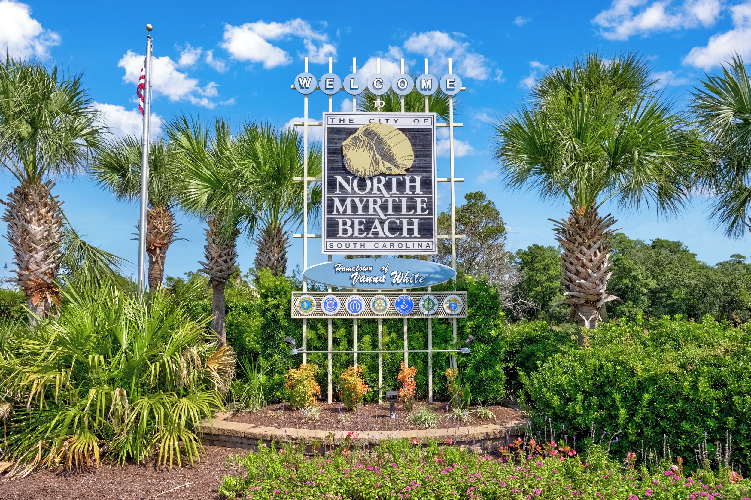 A welcome sign for North Myrtle Beach, South Carolina, surrounded by palm trees and a clear blue sky.