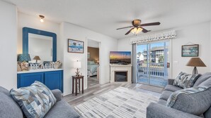 A living room with a fireplace, a ceiling fan, and a view of the outside. - Affordable cozy 2 bedroom condo 1st floor screened in patio in gated community. (North Myrtle Beach)