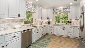 Uma cozinha moderna com armários brancos, eletrodomésticos de aço inoxidável e um tapete estampado em tons de verde.