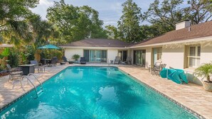 Piscina retangular com borda azulejada, rodeada por espreguiçadeiras e um espaço coberto com varanda.