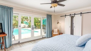 Quarto com uma cama grande, ventoinha no teto e porta de vidro que dá para uma área de piscina.