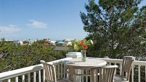 A round wooden table with four chairs, a vase with flowers, and a view of the ocean and buildings in the background. - 5-bedroom Home just 4.5 min walk to Dedicated Private Beach & 2 community pools (Santa Rosa Beach)