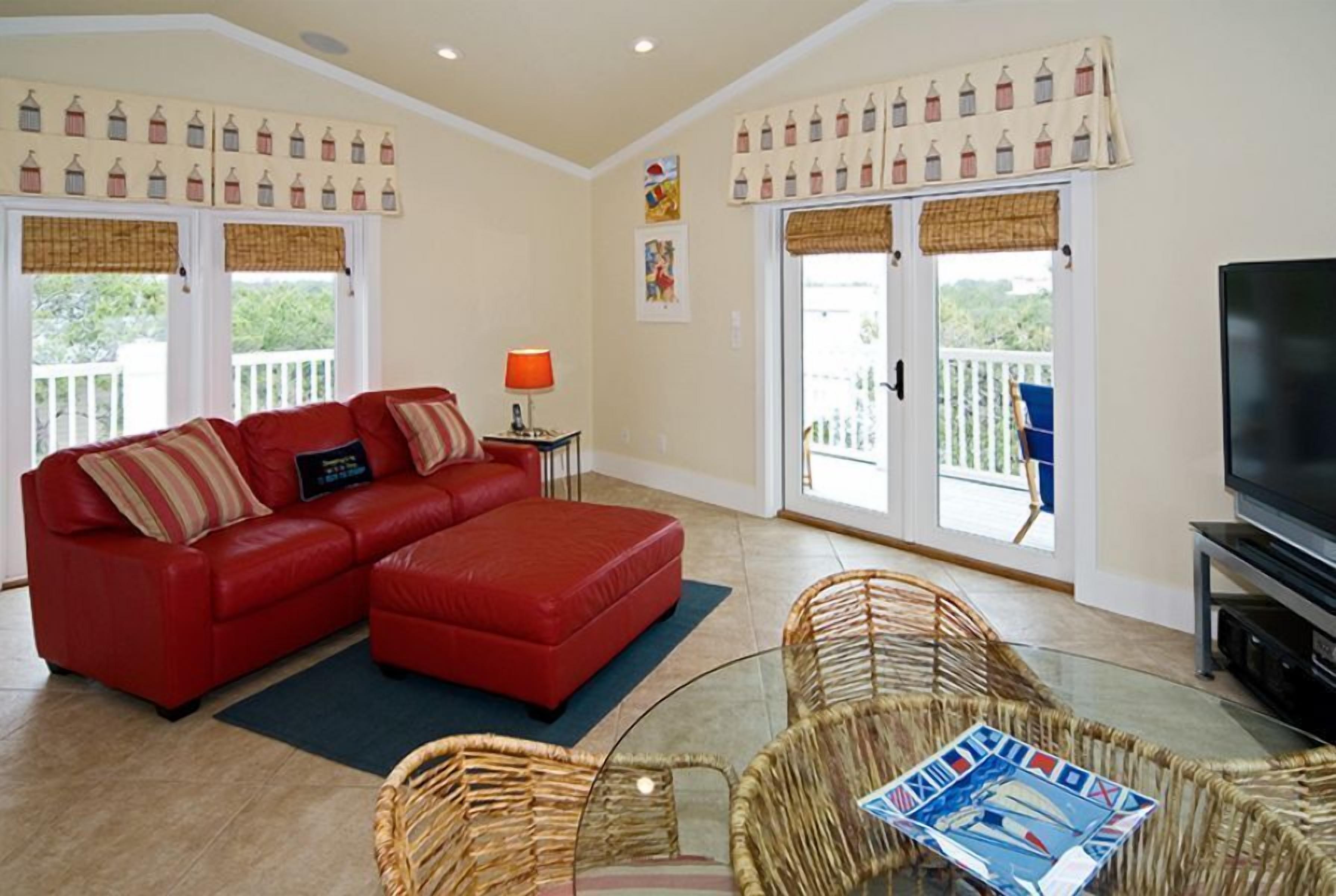 A living room with a red sofa, wicker chairs, a TV, and a balcony with a view.