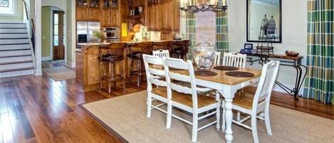 A spacious kitchen with wooden cabinets, a dining area with white chairs, and a chandelier.