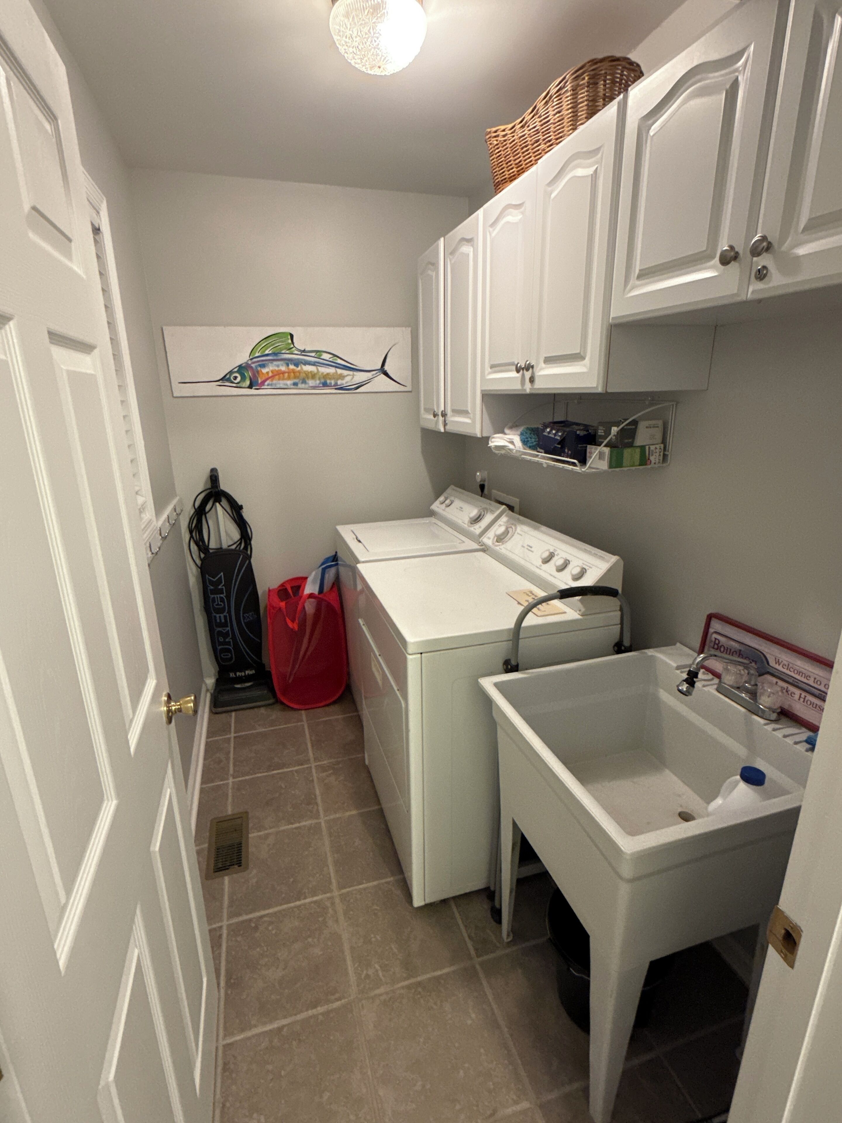 Une buanderie équipée d’un lave-linge, d’un sèche-linge, d’un évier et d’un panier fixé au mur.