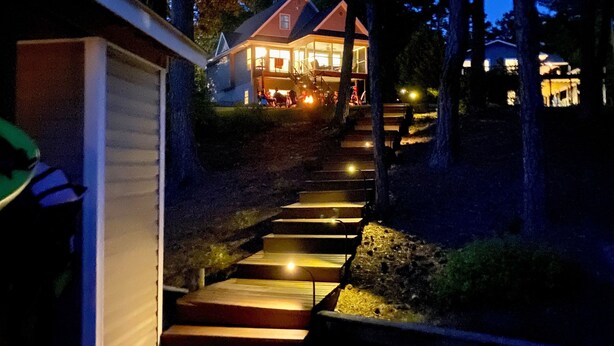 Uma casa com escadaria de madeira que leva a uma entrada iluminada, cercada por árvores.