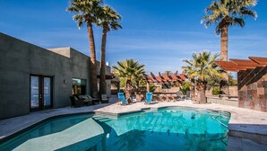 A swimming pool with lounge chairs and palm trees, surrounded by a modern building with a red-tiled roof.