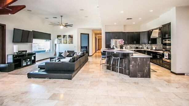 A modern kitchen with dark cabinetry, a central island, and a dining area with a sofa and chairs.