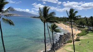 A beach with clear turquoise water, palm trees, and a distant mountain range. - Royal Mauian Oceanfront, Fabulous View!   (Kihei)
