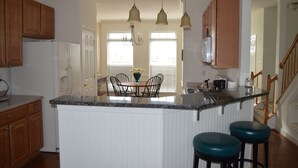 A kitchen with wooden cabinets, a central island with stools, a chandelier, and a view to a dining area.