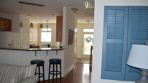 A kitchen with a central island, wooden cabinets, and pendant lighting. There is a bar stool and a striped sofa in the foreground.