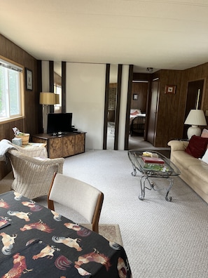 A spacious living room with a large window, a television, a glass coffee table, and a sofa. - Private Beach Access Trail, peaceful wooded setting - sleeps 3 (Port Angeles)