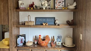 A kitchen shelf with various items including a 'FARM FRESH' sign, a 'FRESH EGGS' sign, a framed chicken illustration, and a 'Whales' magazine.