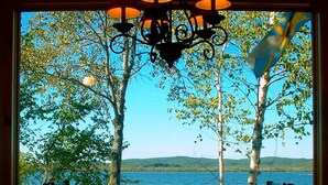 Un comedor con vistas a un lago y árboles, un candelabro y una mesa con sillas.